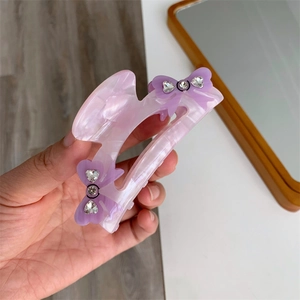 Detail of purple marble acetate hair claw with rhinestone bow accents held in hand