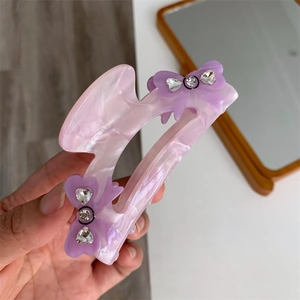 Close-up of pink marble acetate hair claw clip with purple rhinestone bows detail