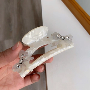 Close-up of cream white marbled acetate hair claw clip with crystal bow detailing