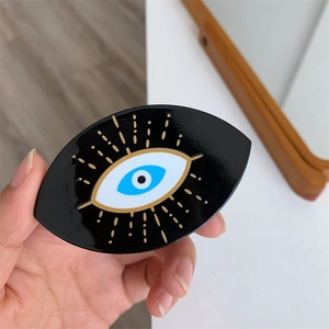 Dettaglio del supporto per telefono Evil Eye con raggi dorati tenuto in mano