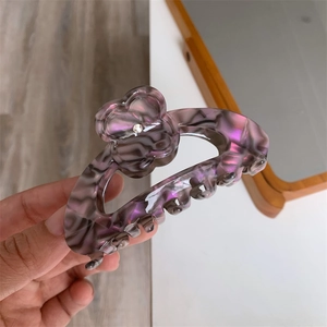 Detail of purple acetate flower hair claw clip with marble texture and rhinestone center