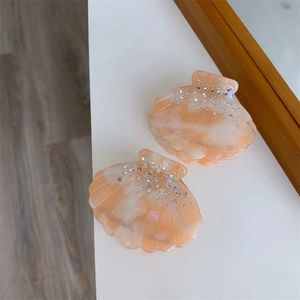 Vue détaillée des pinces à cheveux marbrées en forme de coquillage avec strass ton pêche