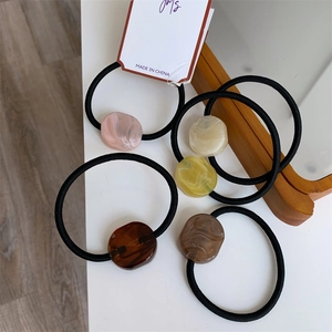 Five elastic hair ties with marble-textured acrylic beads on a minimalist wood background