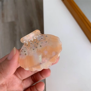 Détail d'une pince à cheveux en acétate en forme de coquillage rose nacré avec strass