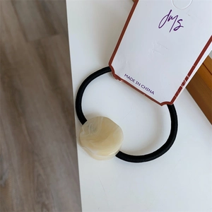 Detail of high-elastic black hair tie with marble textured bead and product tag