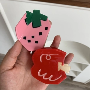 Detailed view of glossy strawberry and cherry shaped hair claws in hand for size comparison