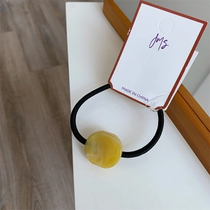 Macro shot of a yellow resin bead hair tie with marble texture on a white display card