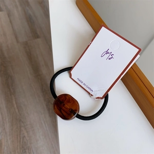 Detail view of a black high-elastic hair tie with an amber resin accent on a white card