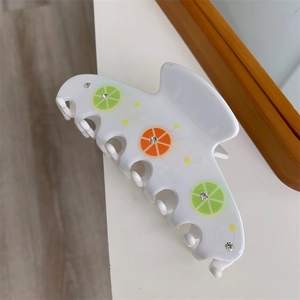 Detail of white acetate hair claw clip featuring lemon fruit patterns and rhinestones