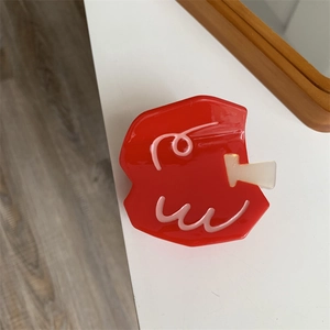 Detail view of red fruit-style hair claw clip with pink wavy patterns on a white table