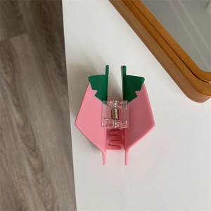 Close-up of a pink and green fruit style matte hair claw clip on a white table surface