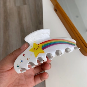 Close-up detail of white acetate shark hair claw clip with rainbow and star rhinestone decor