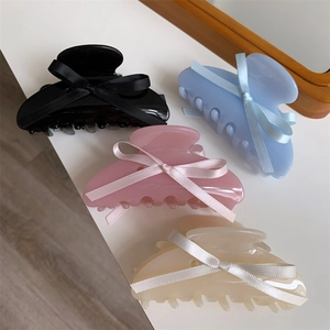 Détail de quatre pinces à cheveux en acétate avec nœuds en noir, bleu, rose et crème