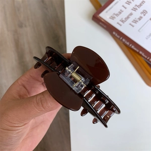 Detailed view of a dark brown glossy resin hair claw clip held in hand over a desk