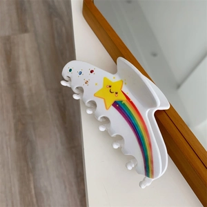 Close-up of a white acetate star hair claw with rainbow stripes and colorful rhinestones
