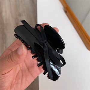 Détail d'une pince à cheveux noire brillante avec un élégant nœud en ruban à la main
