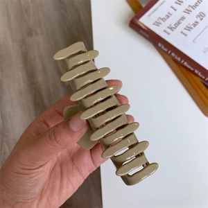 Detail of a large khaki hair claw clip with golden logo held against a book background