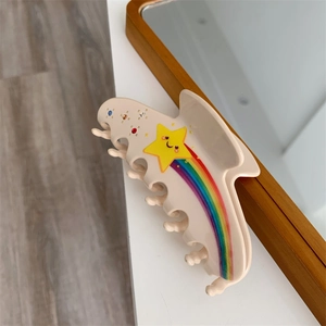 Close-up of cream hair claw clip with rainbow star motifs and colorful rhinestones