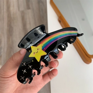 Close-up of black acetate hair claw featuring rainbow stripes and a smiling yellow star