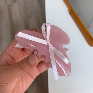 Détail d'une pince à cheveux en acétate rose pâle avec un nœud en ruban de satin blanc