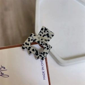 Detail view of mini hair claw clip featuring black and white spotted cow pattern texture