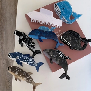 Détails de pinces à cheveux en acétate motif baleine et requin sur un livre rose