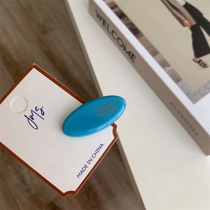 Polished bright blue acetate hair clip with gold lettering on a minimalist card