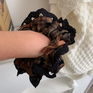 Close-up of brown plaid scrunchie with black lace trim and silk bows on a wrist
