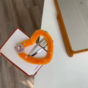 Dettaglio del fermaglio a cuore di peluche arancione con gemma rosa e paillettes