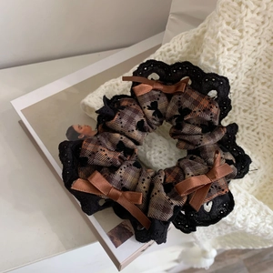 Detail of dark brown plaid hair scrunchie with lace edges and ribbon bows on white knit fabric