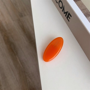 Detail of bright orange handmade acetate hair clip with polished resin finish on a white stand