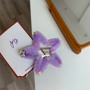 Macro di una molletta a stella in peluche viola con paillettes e ciondolo a stella piccolo