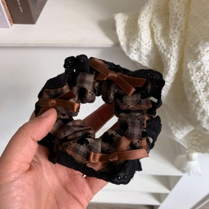 Detail of checkered scrunchie with lace trim and brown satin bows in hand-held close-up