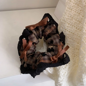 Close-up of brown plaid scrunchie with delicate black lace trim and satin bows