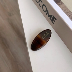 Detailed macro view of an oval acetate hair clip with tortoise shell pattern and gold lettering