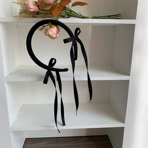 Close-up of black ballet-style headband with long ribbon bows hanging on a white rack