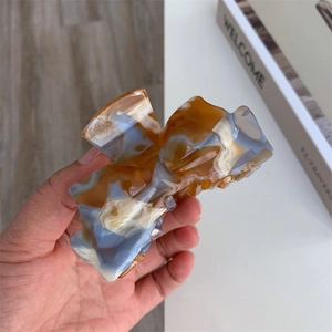 Close-up of marble acetate hair claw clip with amber and blue patterns held in hand