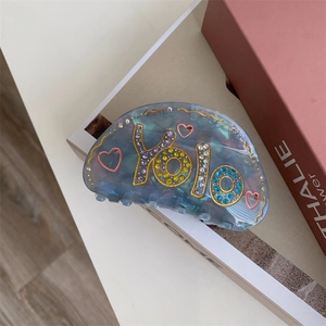 Détail de la pince à cheveux bleue en acétate avec lettrage YOLO en strass et bord doré