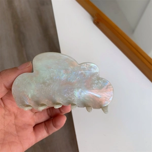 Detail of cloud-shaped acetate hair claw with iridescent pearlescent finish held in hand