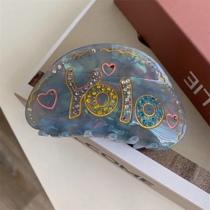 Pince à cheveux en acétate bleu iridescent avec lettrage YOLO en strass et motif cœur