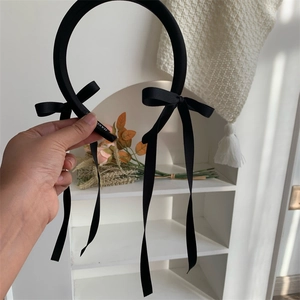 Macro detail of handmade black satin headband featuring long ribbon bows and woven label