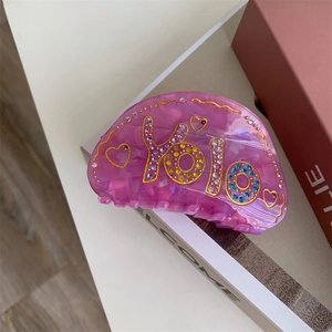Détail d'une pince à cheveux dégradée ornée de strass colorés et du lettrage yolo gravé