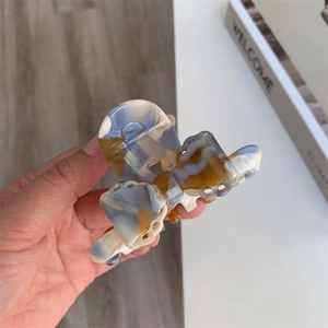 Macro shot of 3D dog-bow hair claw clip with amber marble texture and spring mechanism