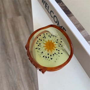 Detailopname van een kiwi-vormige haarklem met realistisch zadenpatroon op een witte tafel