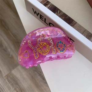 Détail de la pince à cheveux rose translucide avec strass YOLO et motif cœur