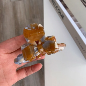 Detail view of bow-shaped acetate hair claw with amber tortoiseshell pattern held by hand