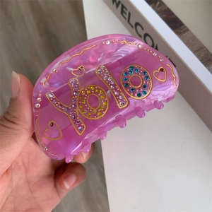 Détail de la pince à cheveux en acétate rose avec lettrage YOLO et strass colorés