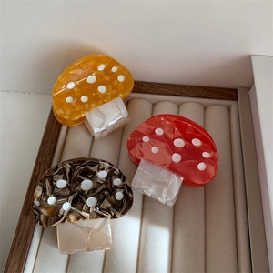 Three colorful mushroom hair claws in orange and red on a velvet jewelry display tray