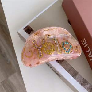 Détail de la pince à cheveux en acétate rose avec lettrage YOLO en strass multicolores
