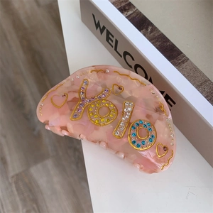 Détail de pince à cheveux en acétate rose avec strass YOLO et motifs de cœur dorés